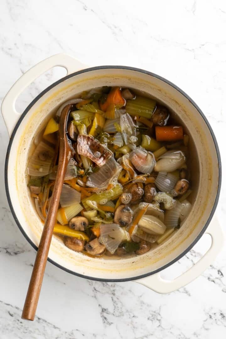 Overhead view of finished vegetable broth in pot with wooden spoon