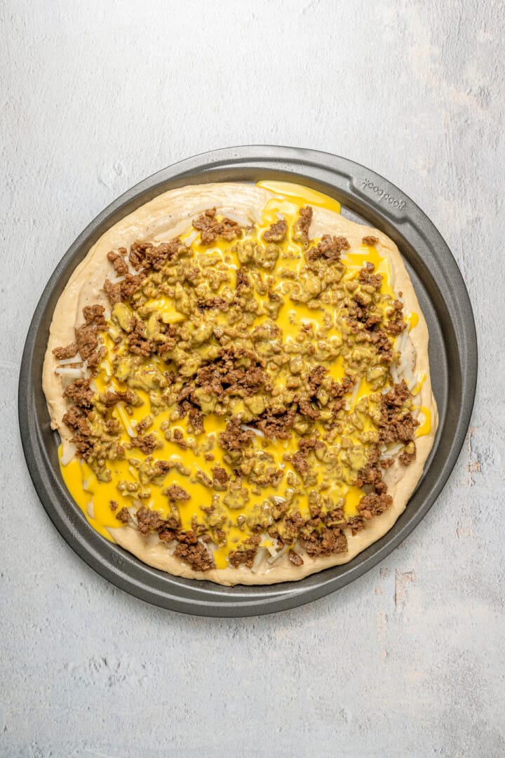 Overhead view of unbaked vegan breakfast pizza after adding egg, sausage, and potatoes