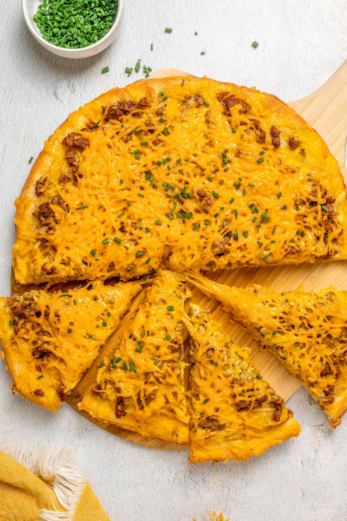 Overhead view of vegan breakfast pizza on wood board, with four slices cut