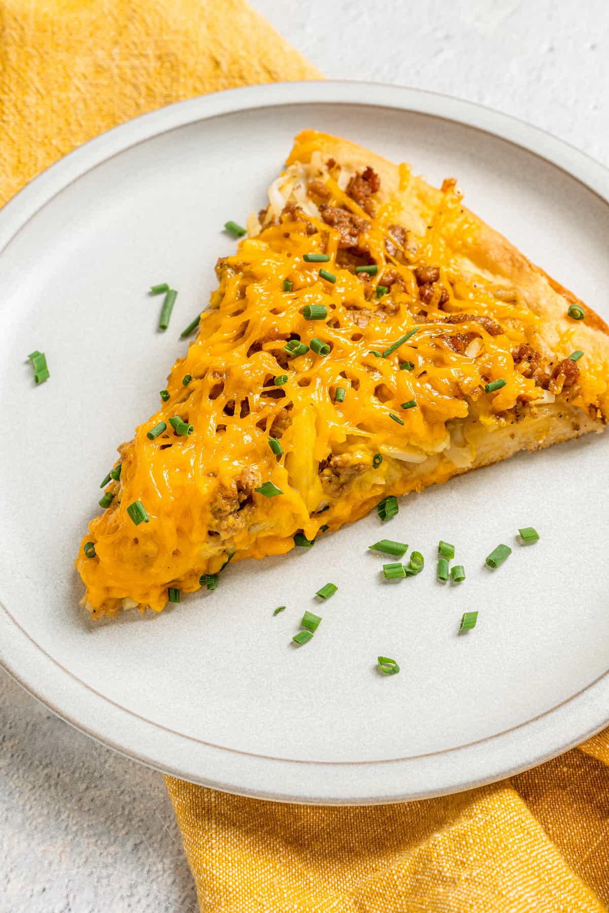 Vegan breakfast pizza slice on white plate, topped with chives