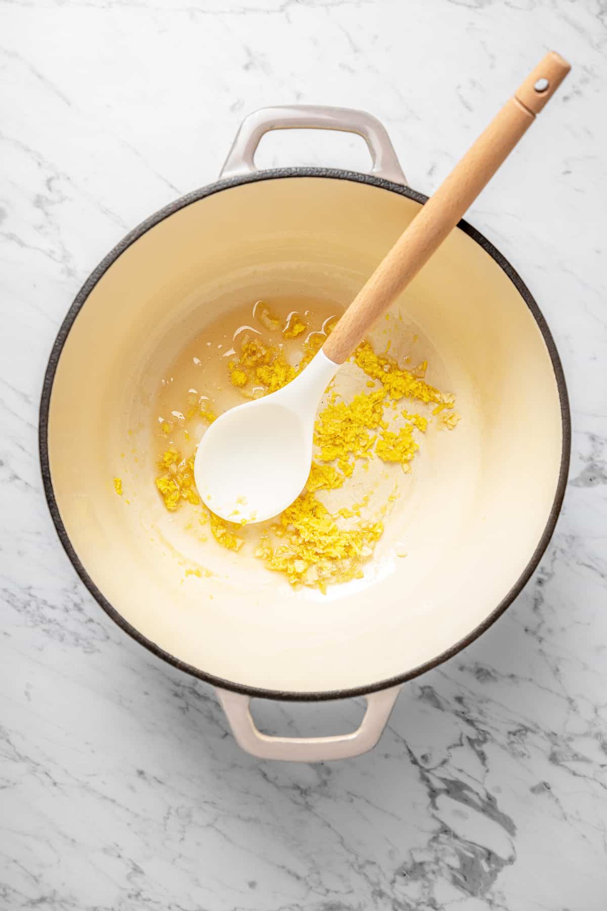 Overhead view of garlic, ginger, and oil in Dutch oven with spoon