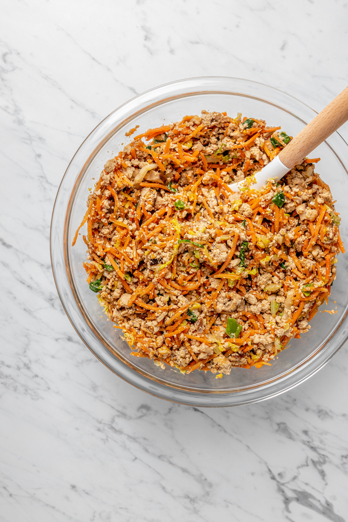 Overhead view of dumpling filling mixture in glass bowl with spoon