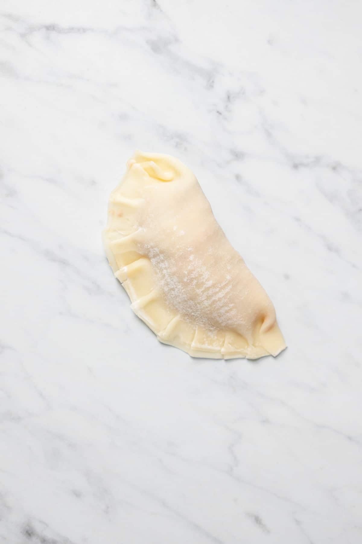 Overhead view of dumpling with crimped edges on marble work surface