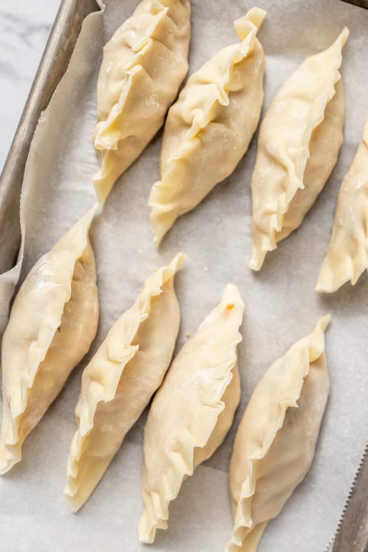 Overhead view of uncooked dumplings on parchment-lined baking sheet