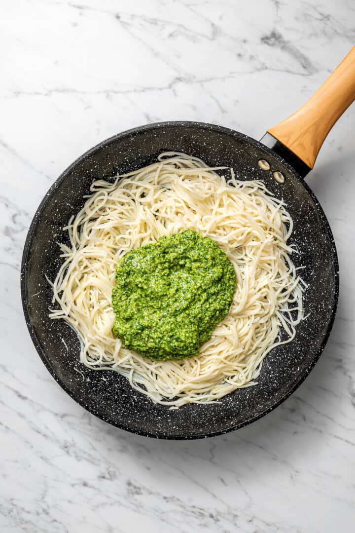 Overhead view of pesto added to skillet of hearts of palm pasta