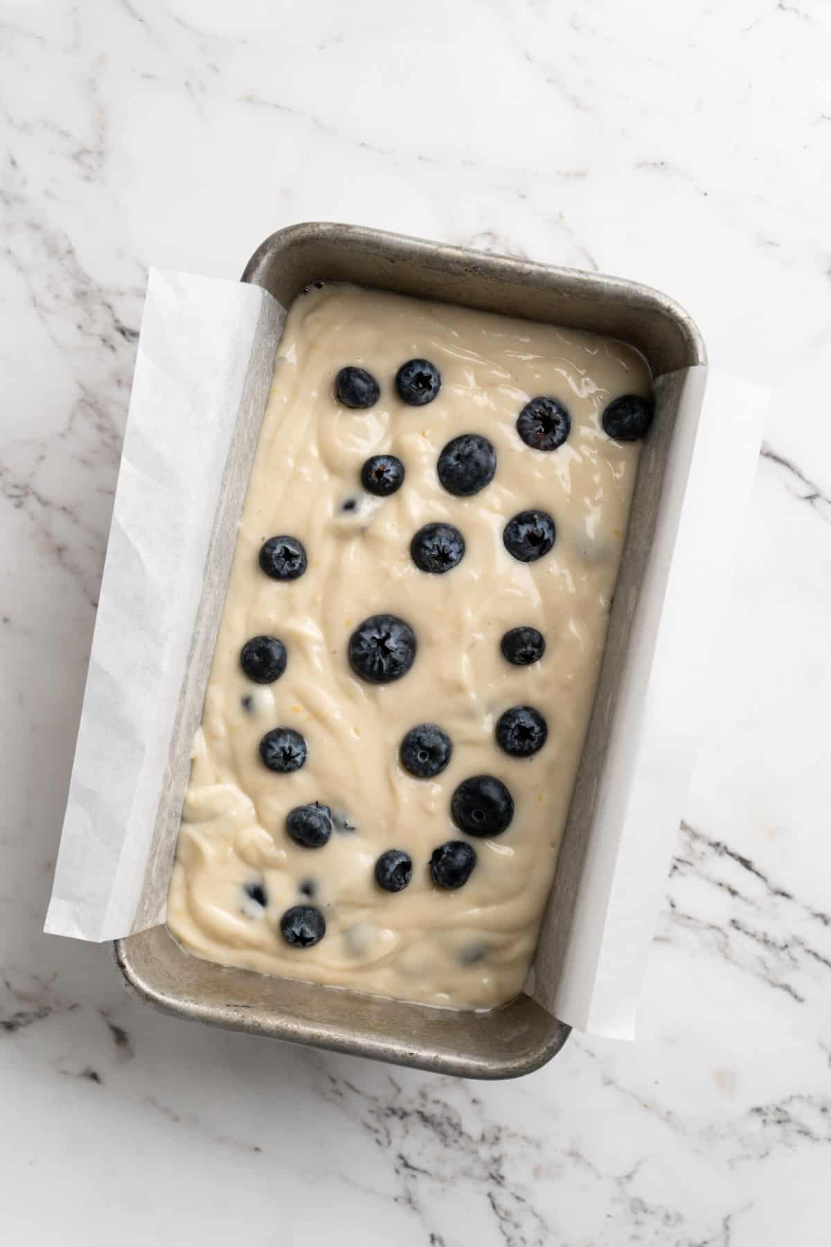 Overhead view of lemon blueberry bread batter in pan with blueberries on top