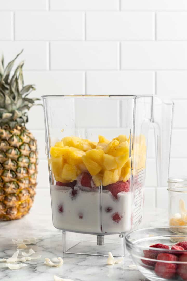 Ingredients for strawberry pineapple smoothie in blender jar