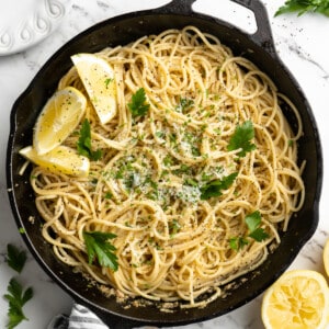 Overhead view of lemon pasta in skillet with lemon wedges and parsley for garnish
