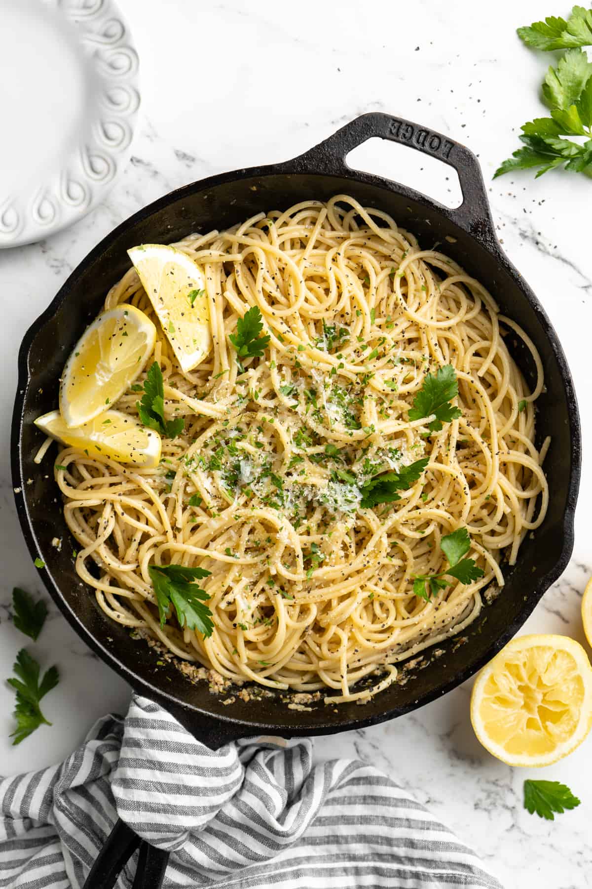 Overhead view of lemon pasta in skillet with lemon wedges and parsley for garnish