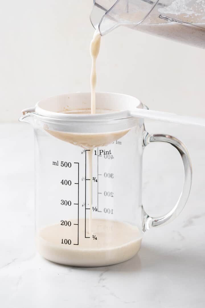 Pouring oat milk coffee creamer through strainer into glass measuring cup