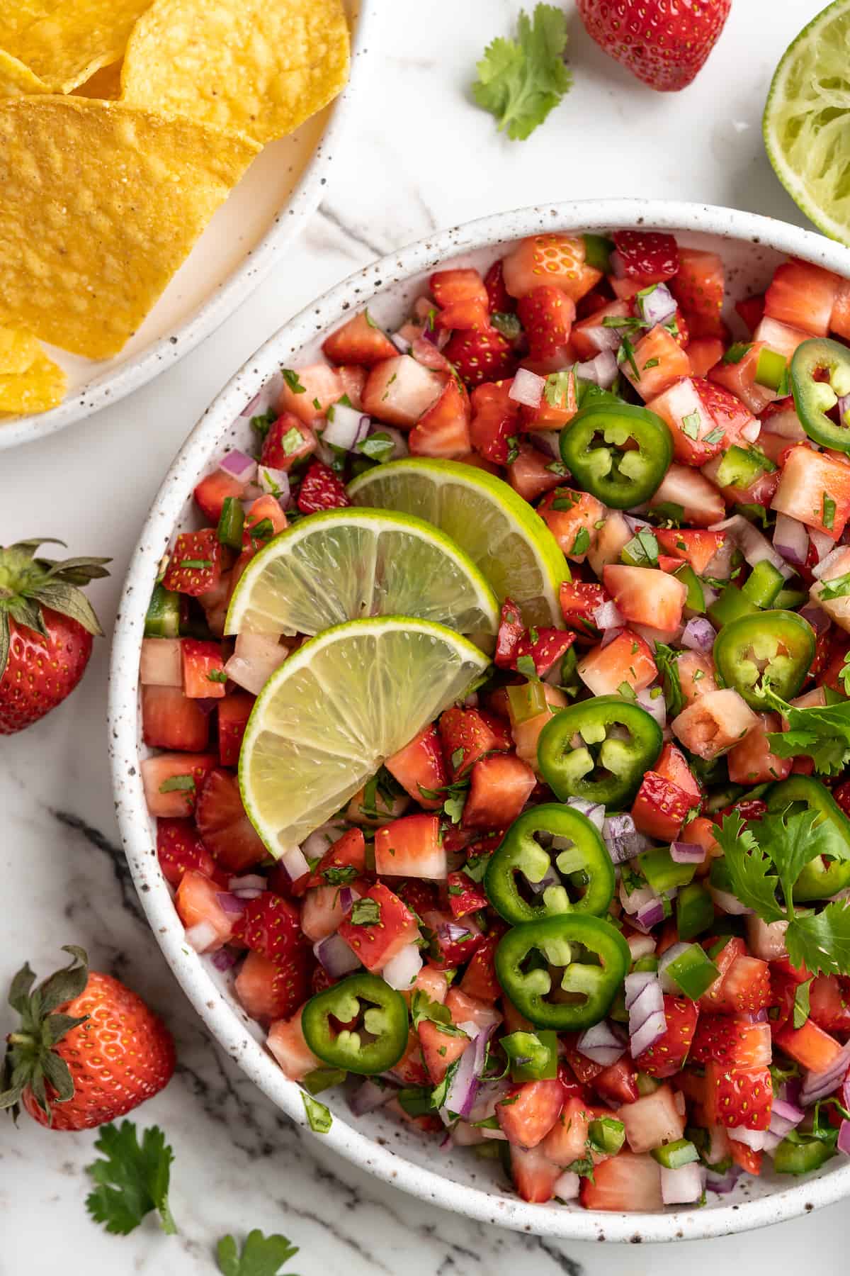 Overhead view of strawberry salsa in bowl with sliced peppers and lime for garnish