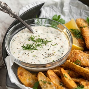 Bowl of tartar sauce garnished with fresh dill on plate of fish and chips