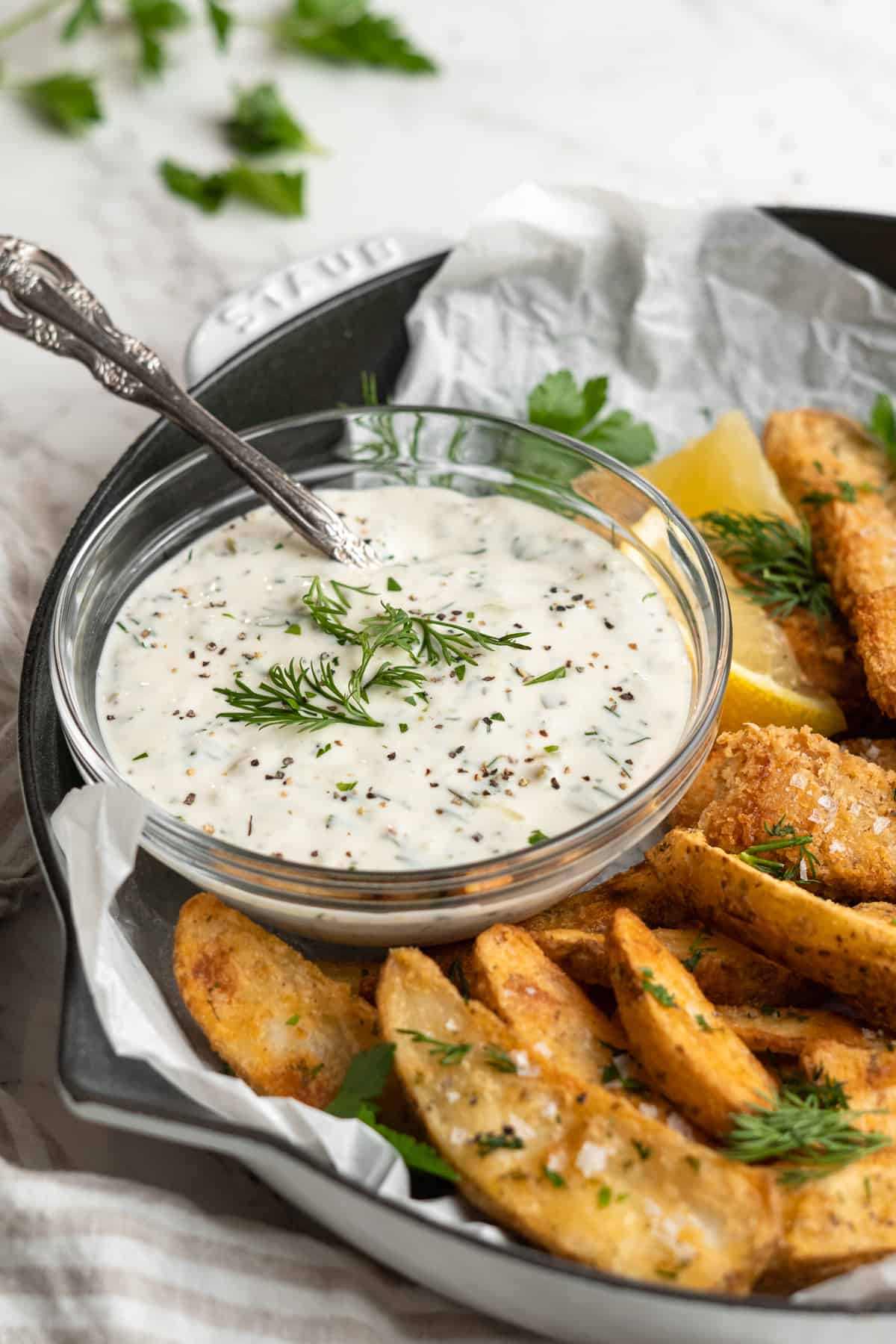 Bowl of tartar sauce garnished with fresh dill on plate of fish and chips