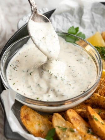 Spoon drizzling vegan tartar sauce back into bowl to show thick texture