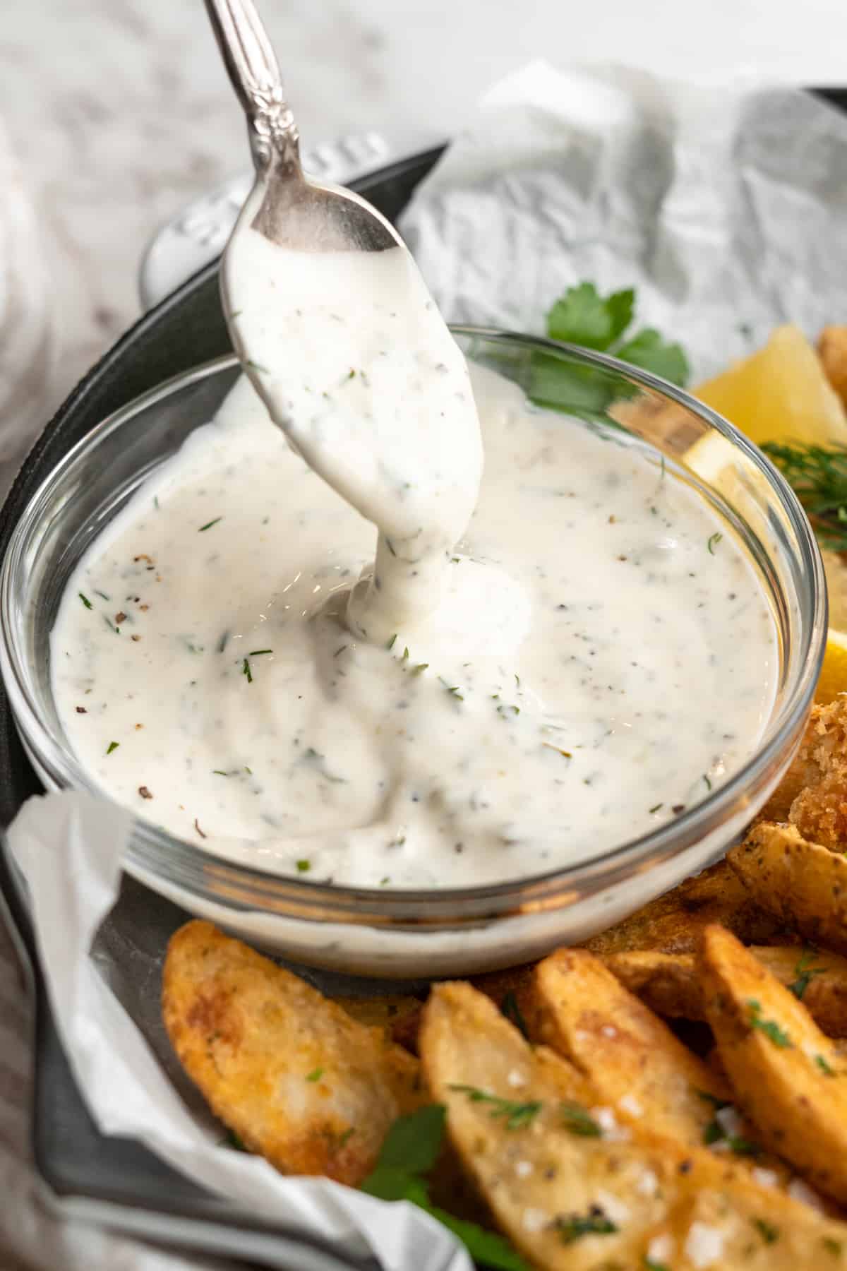 Spoon drizzling vegan tartar sauce back into bowl to show thick texture