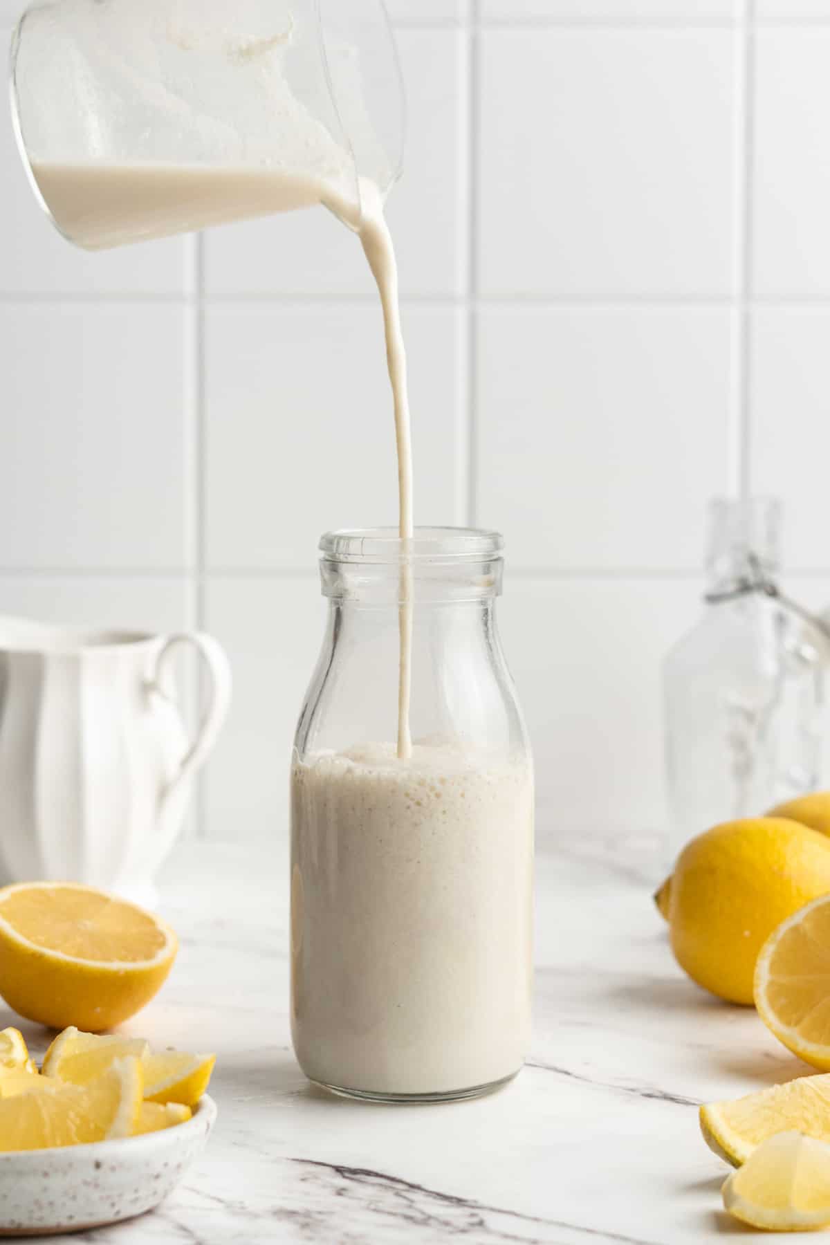 Pouring vegan buttermilk from liquid measuring cup into glass bottle