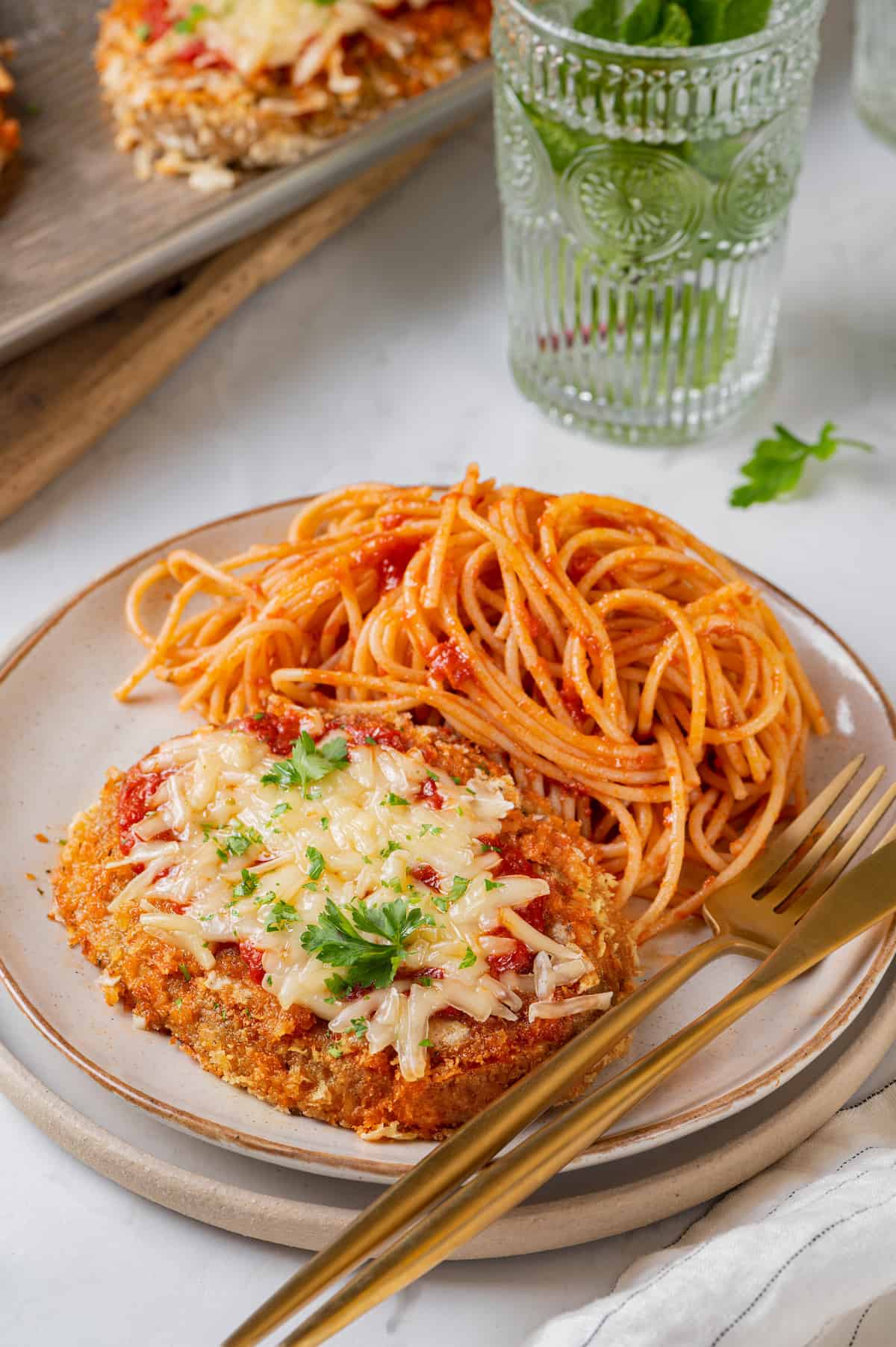 Chicken parmesan on plate with spaghetti, fork, and knife