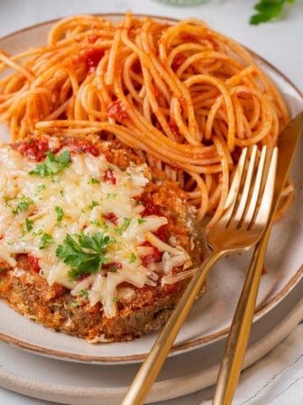 Plate with spaghetti and chicken parmesan, with gold knife and fork set to the side