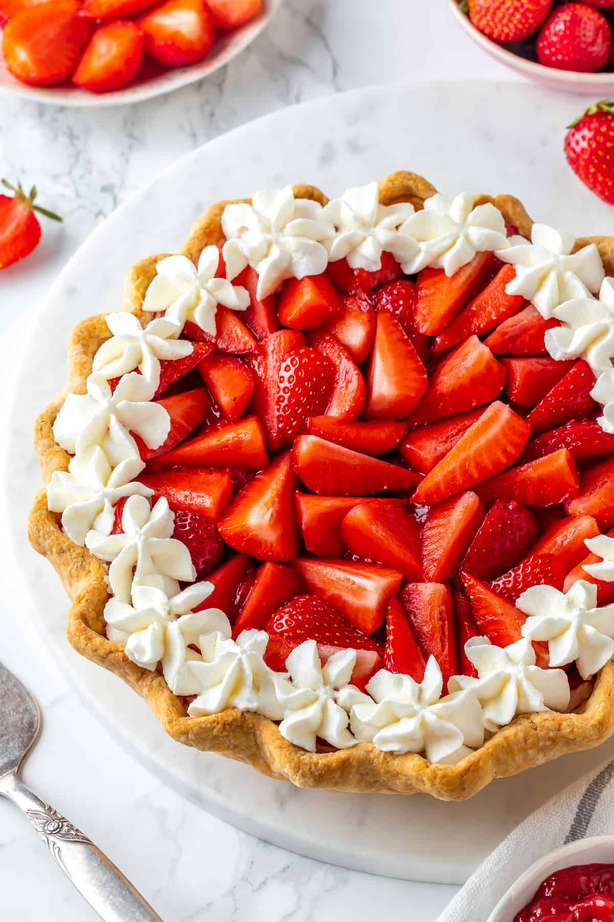 Whole strawberry cream pie surrounded by bowls of fresh strawberries and jam