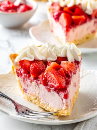 Slice of strawberry cream pie on plate with fork, with another slice of pie in background