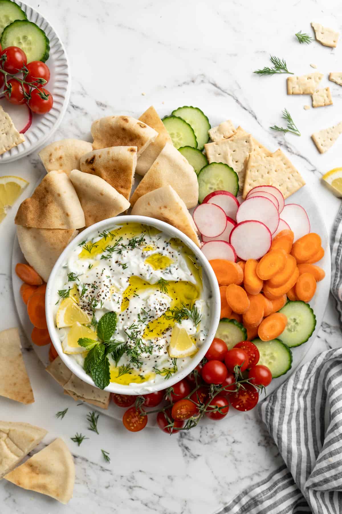 Overhead view of tzatziki in bowl on platter with vegetables, pita, and crackers