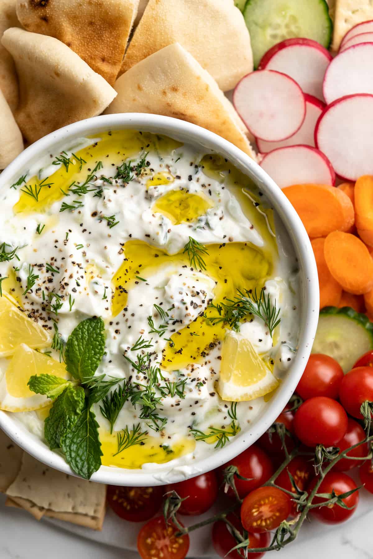 Overhead view of vegan tzatziki in bowl with drizzle of olive oil, fresh herbs, and lemon pieces