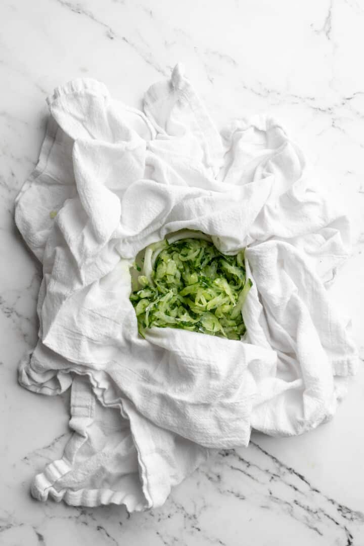 Overhead view of grated cucumber in center of white kitchen towel