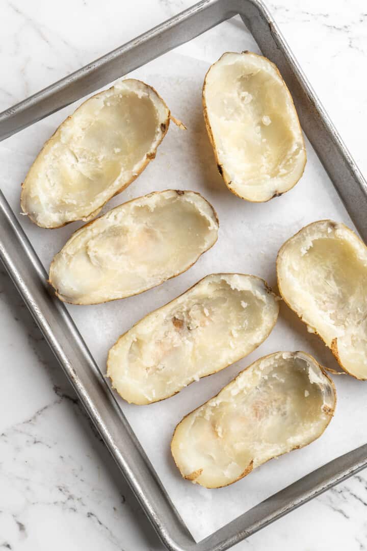 Overhead view of hollowed out potato halves on baking sheet