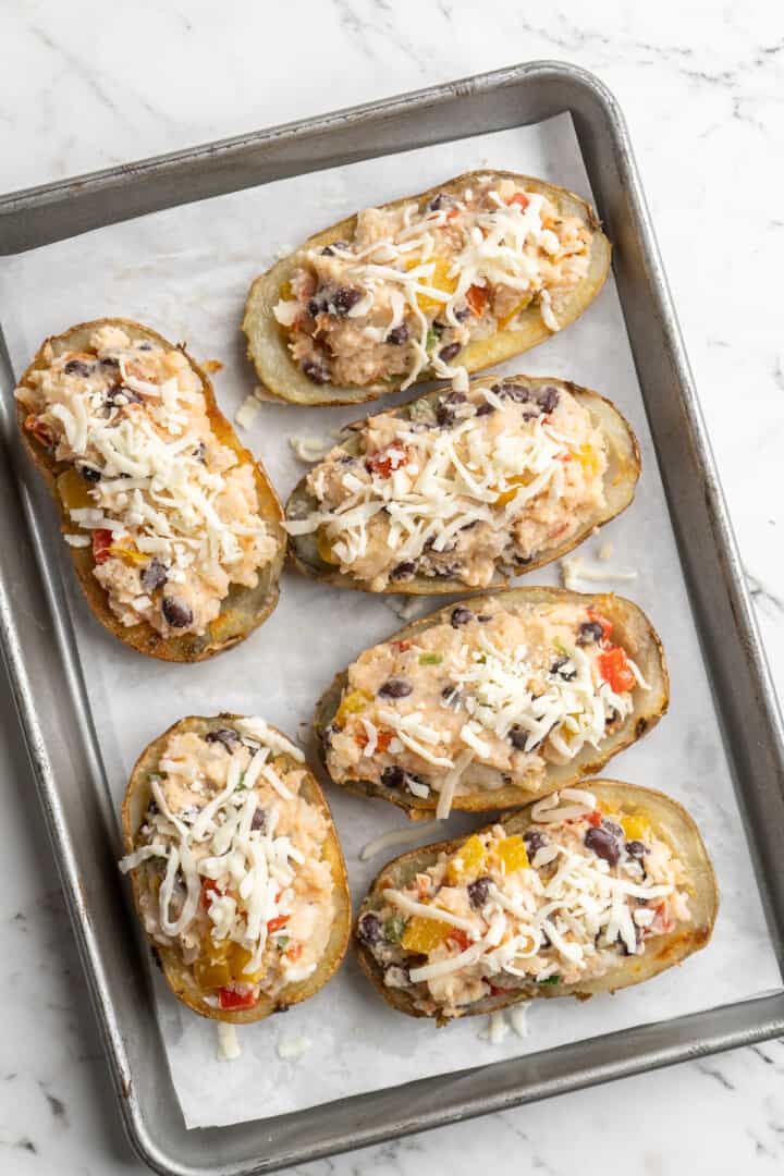 Overhead view of unbaked loaded potato skins on parchment-lined baking sheet