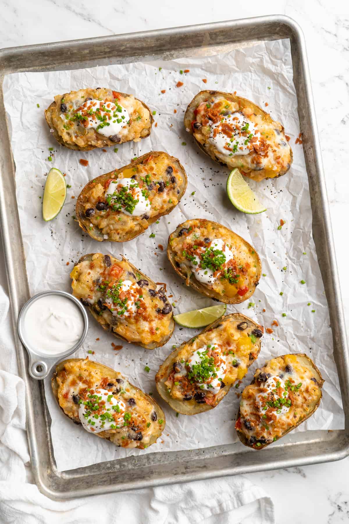Overhead view of loaded potato skins arranged on parchment-lined baking sheet