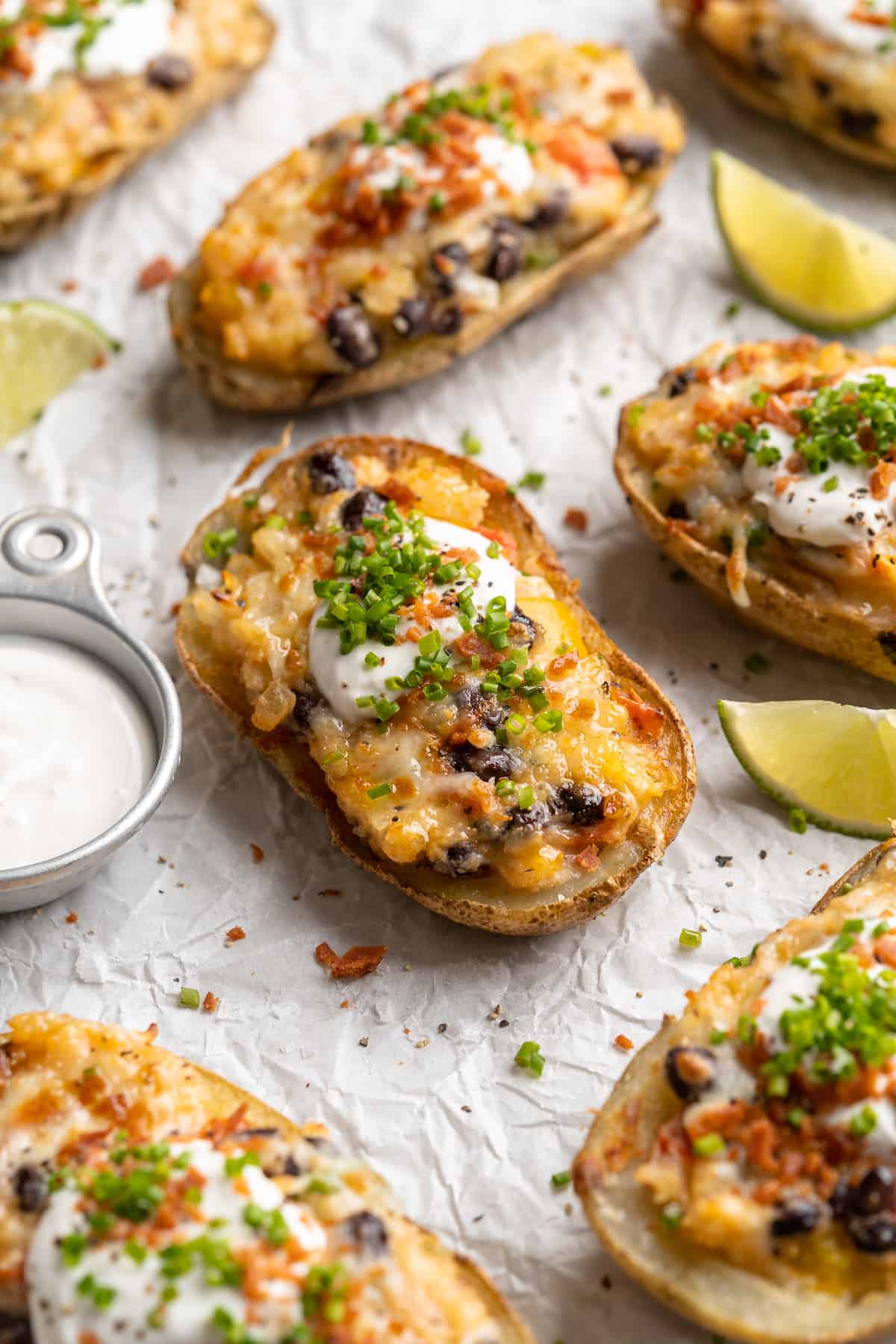 Loaded potato skins on parchment paper with cup of vegan sour cream and lime wedges