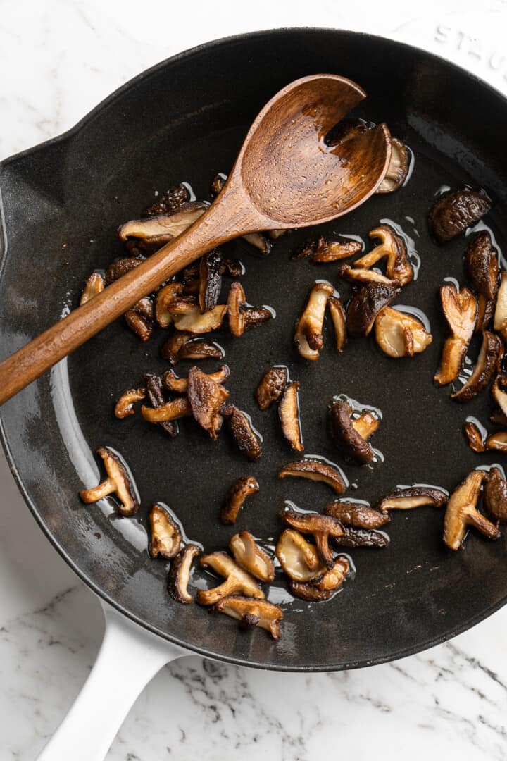 Overhead view of shiitakes cooking in skillet with wooden spoon