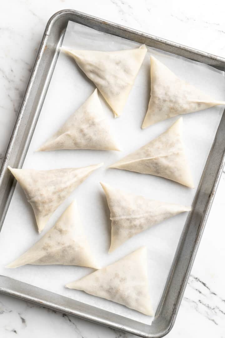 Overhead view of uncooked sambusas on parchment-lined baking sheet
