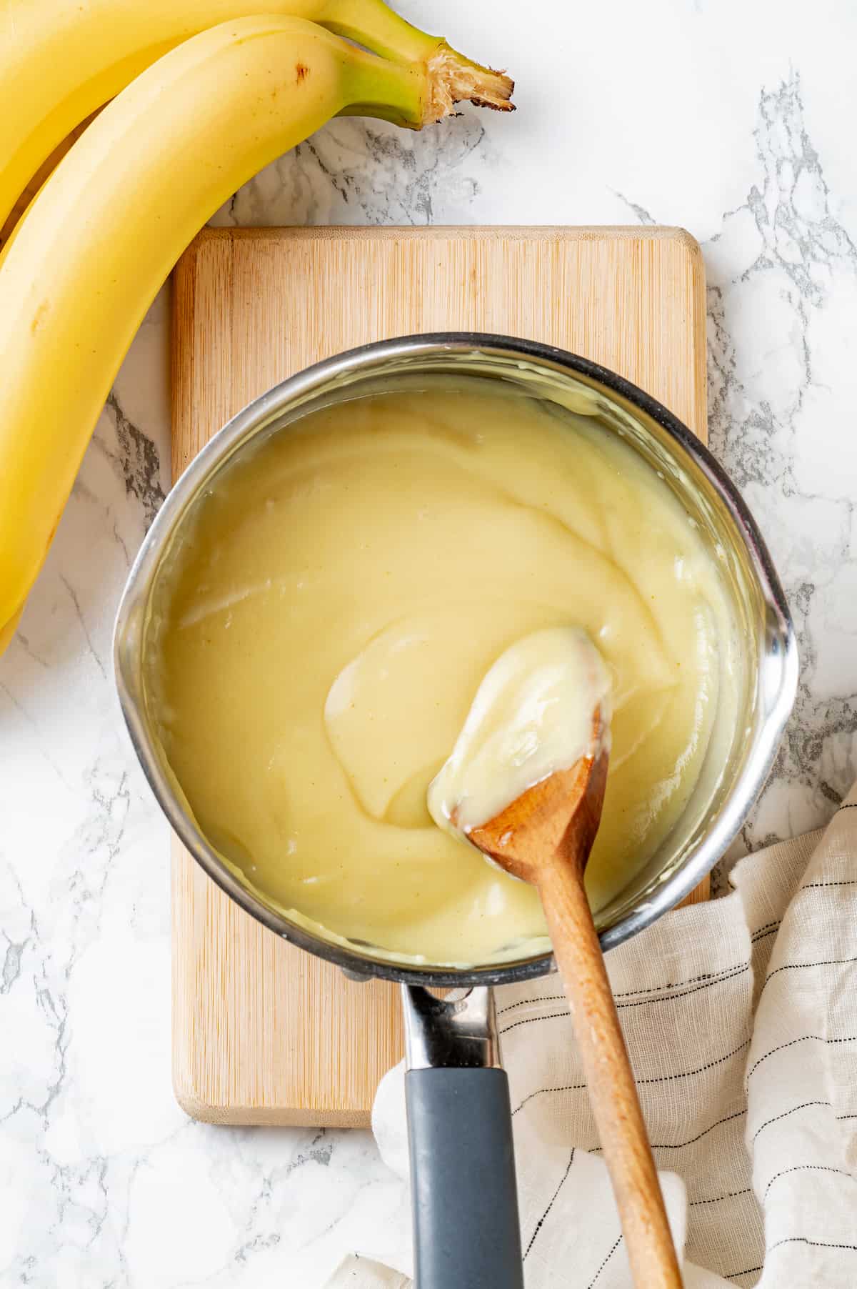 Overhead view of cream filling in saucepan with wooden spoon