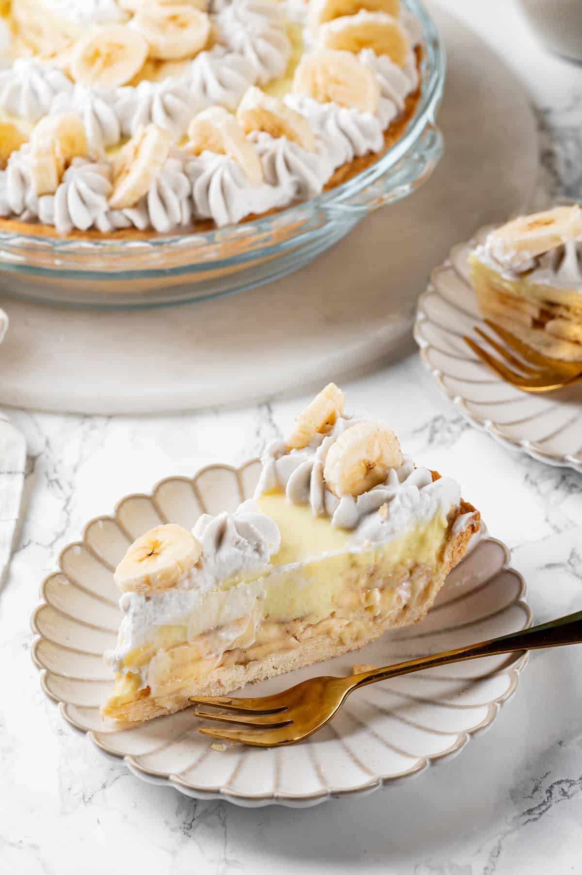 Banana cream pie slice on plate with fork, with remaining pie in background