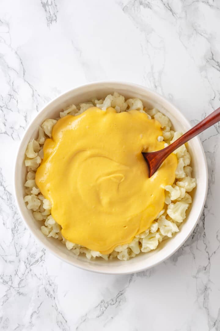 Cheese sauce poured over bowl of cooked cauliflower
