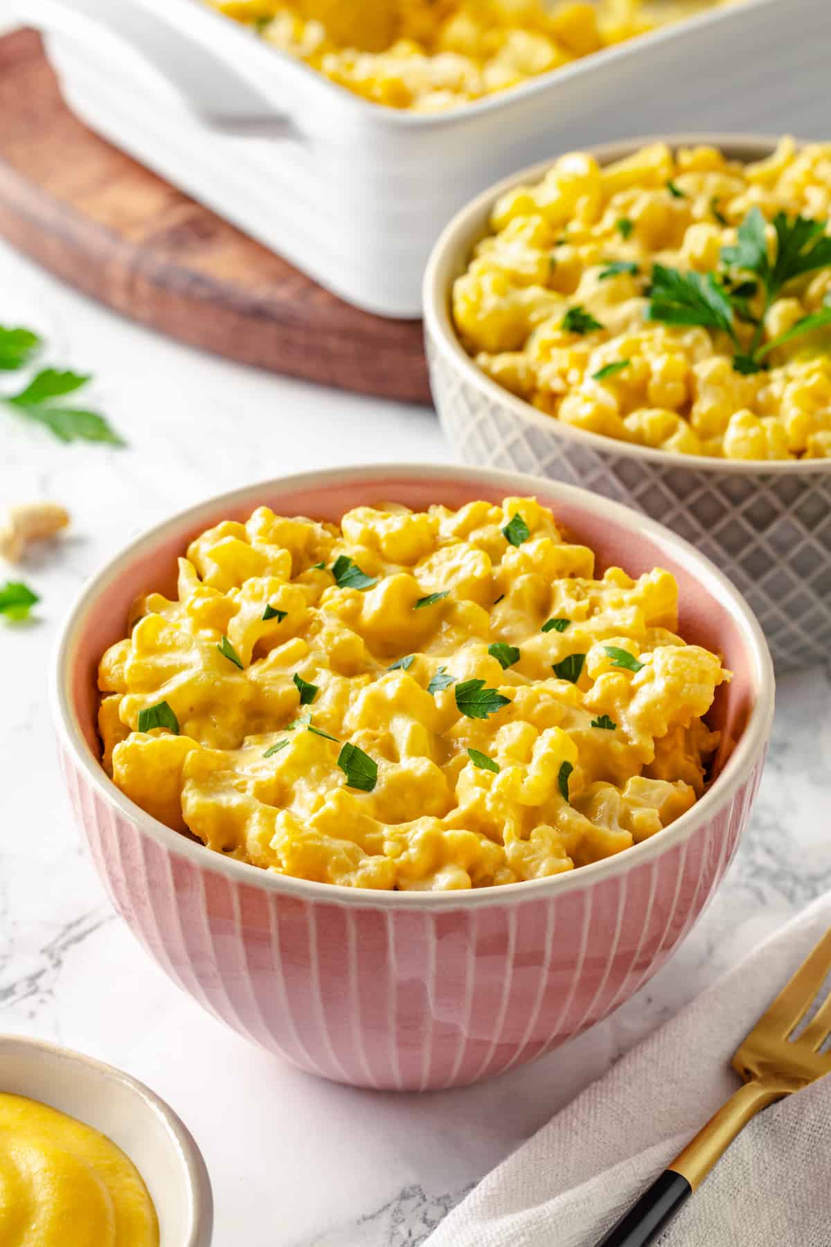 Two bowls of cauliflower mac and cheese with baking dish in background