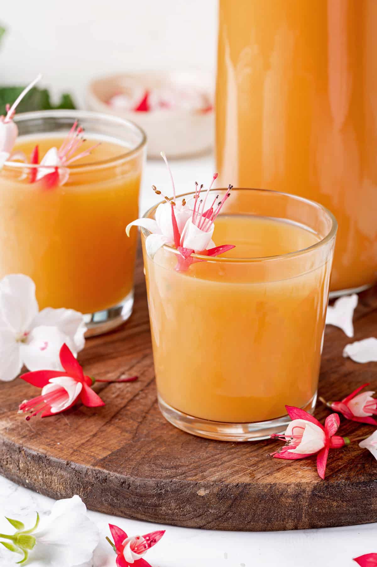 Two juice glasses of POG juice with tropical flowers for garnish