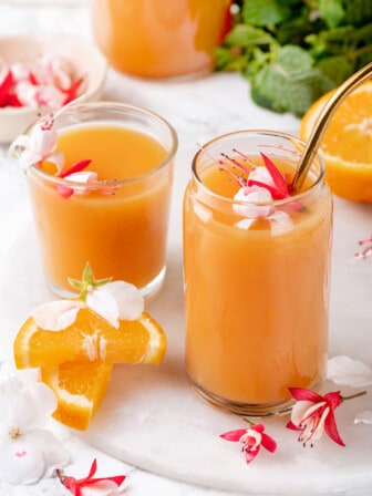 Two glasses of POG juice, one with a straw, and tropical flowers for garnish