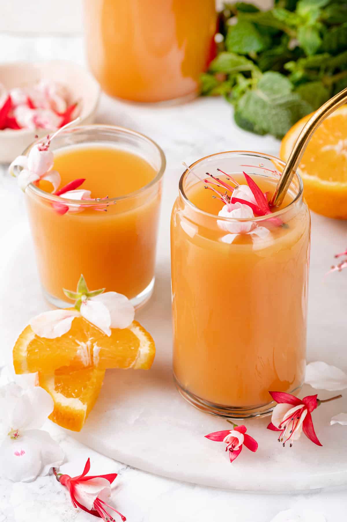 Two glasses of POG juice, one with a straw, and tropical flowers for garnish