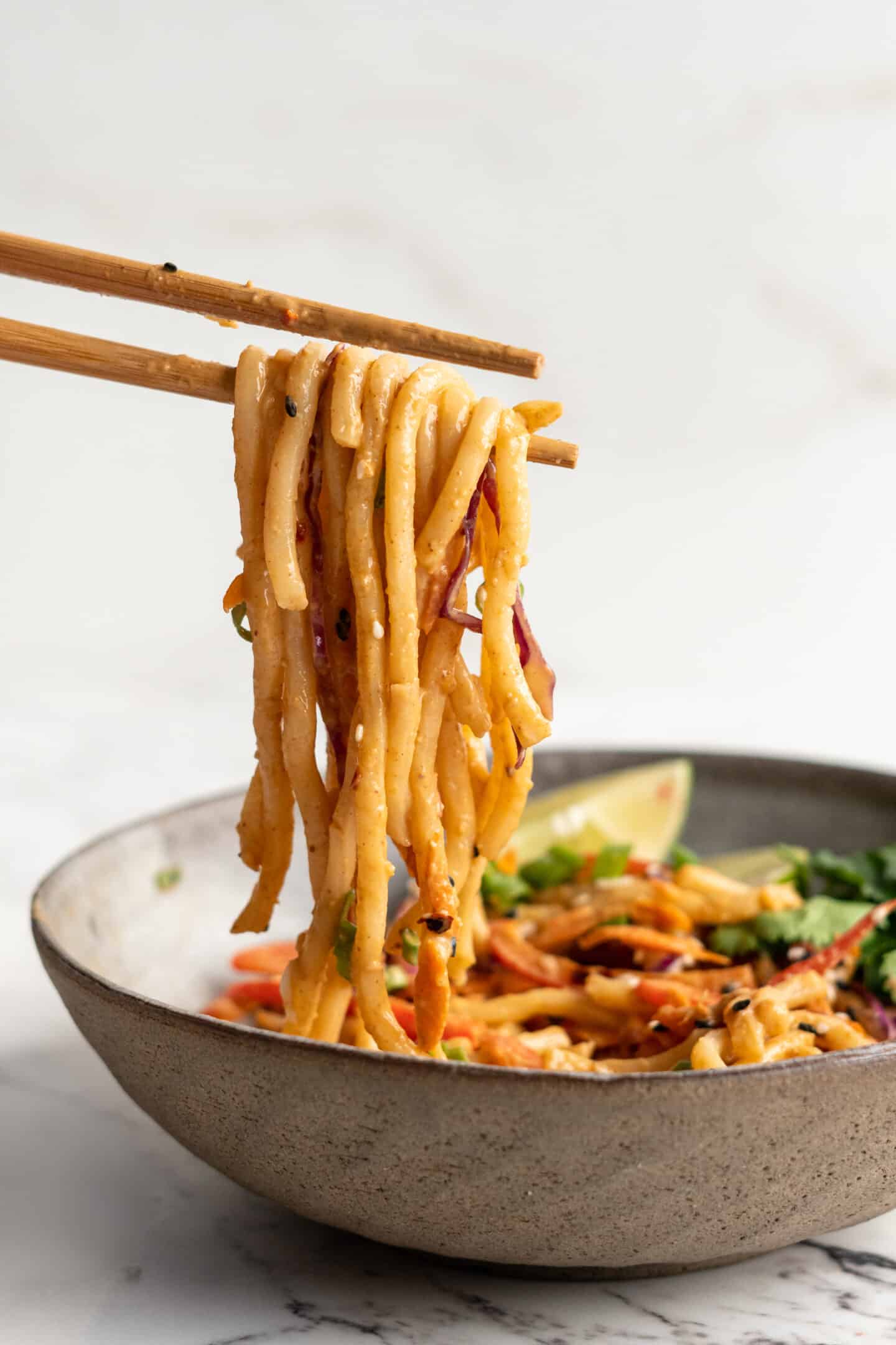 Thai peanut noodles being held with chopsticks above bowl
