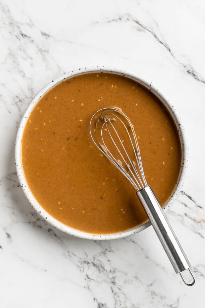 Overhead view of peanut sauce in bowl with whisk