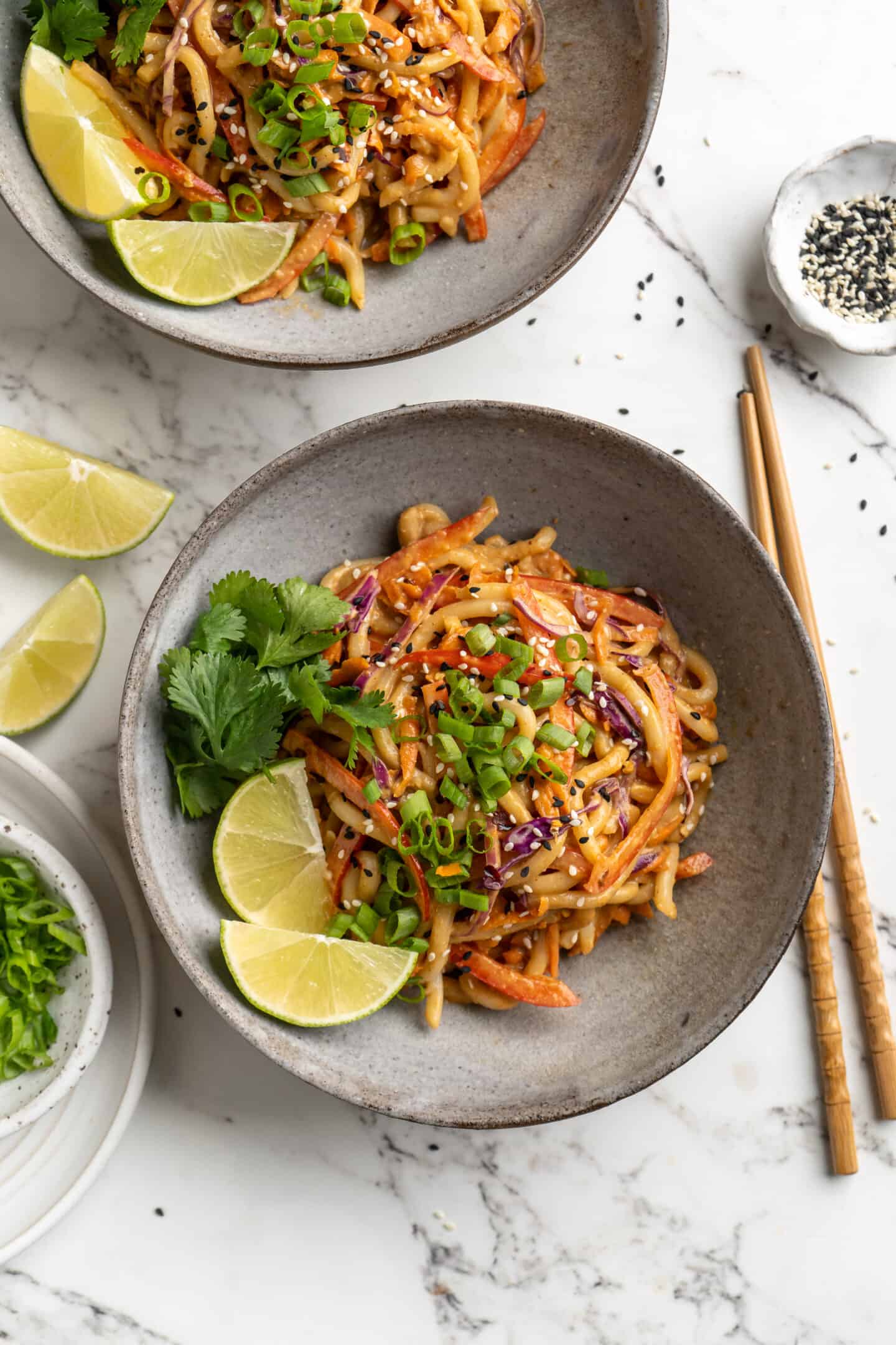 Overhead view of Thai peanut noodles in two bowls set next to chopsticks