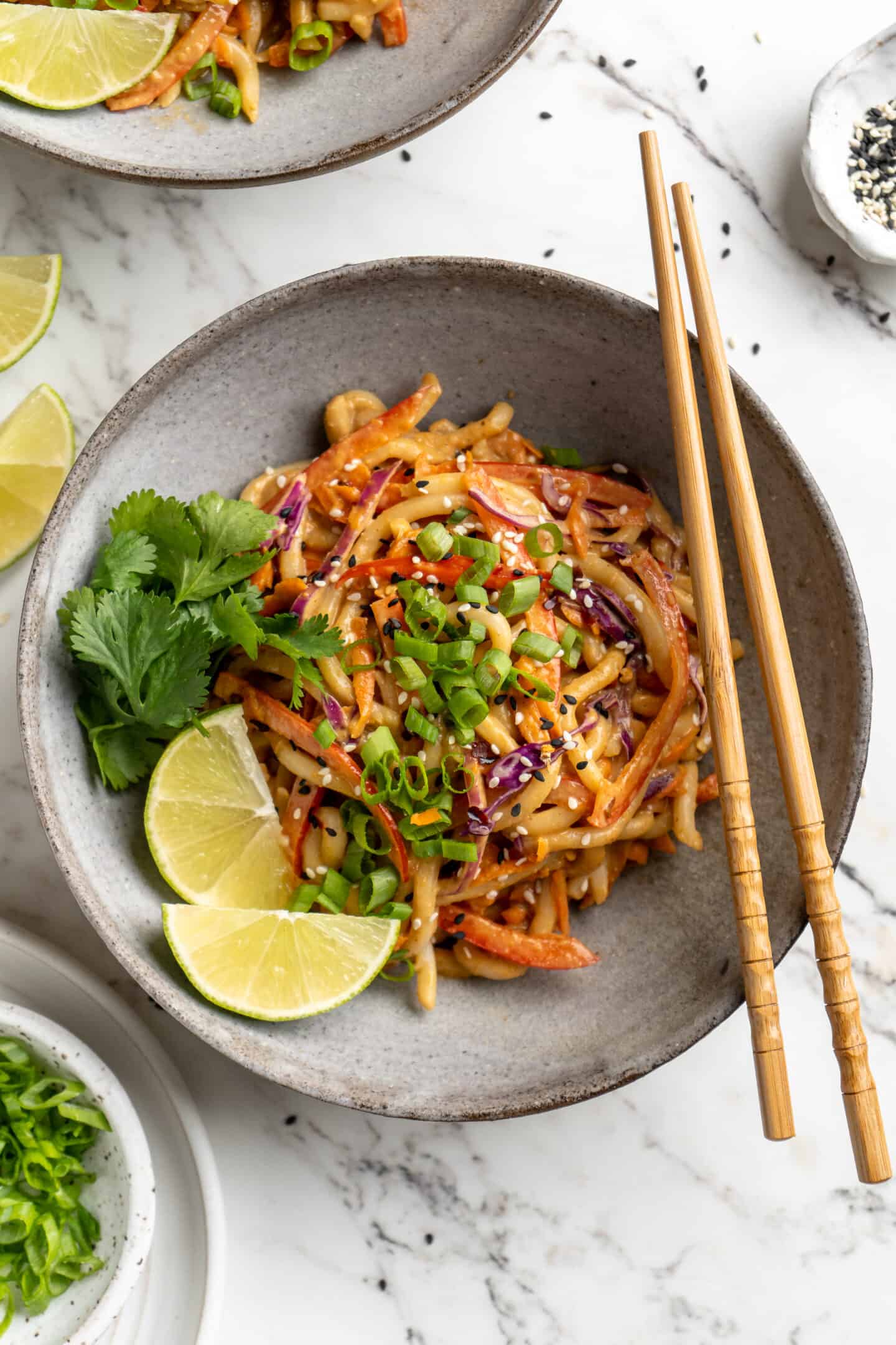 Overhead view of Thai peanut noodles in bowl with lime wedges, cilantro, and green onions for garnish