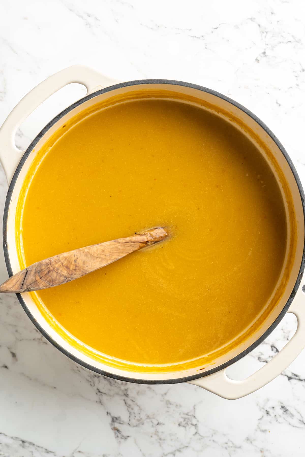 Overhead view of pureed pumpkin soup in pot with wooden spoon