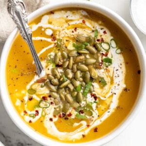 Overhead view of pumpkin soup in bowl with spoon and pepitas, green onions, and coconut cream garnish