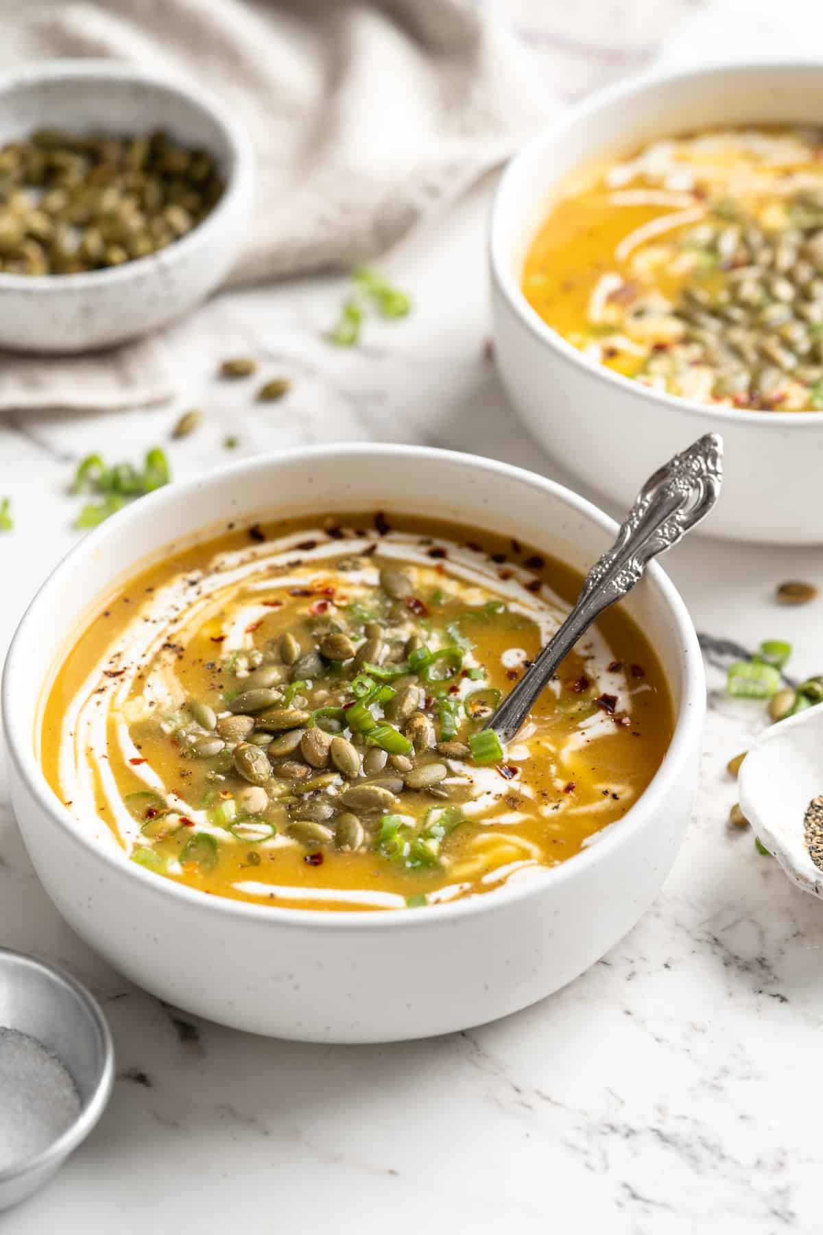 Creamy pumpkin soup in white bowls with pepitas, green onions, and coconut cream garnish