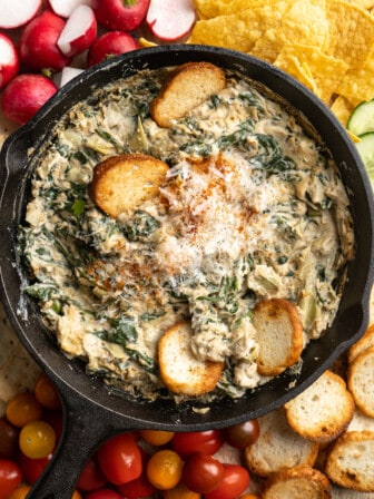 Overhead view of vegan spinach artichoke dip on platter of chips and veggies