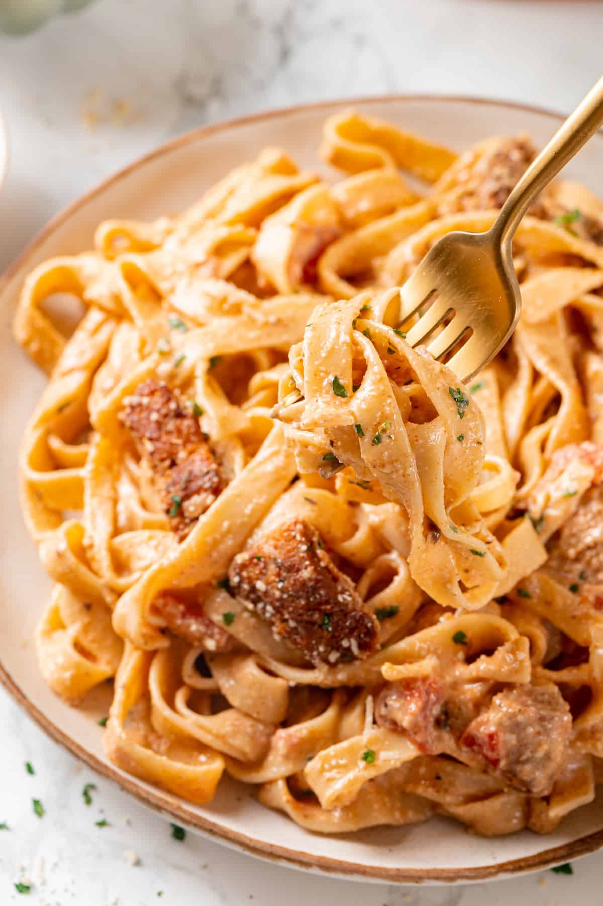 Gold fork holding Cajun chicken pasta over plate