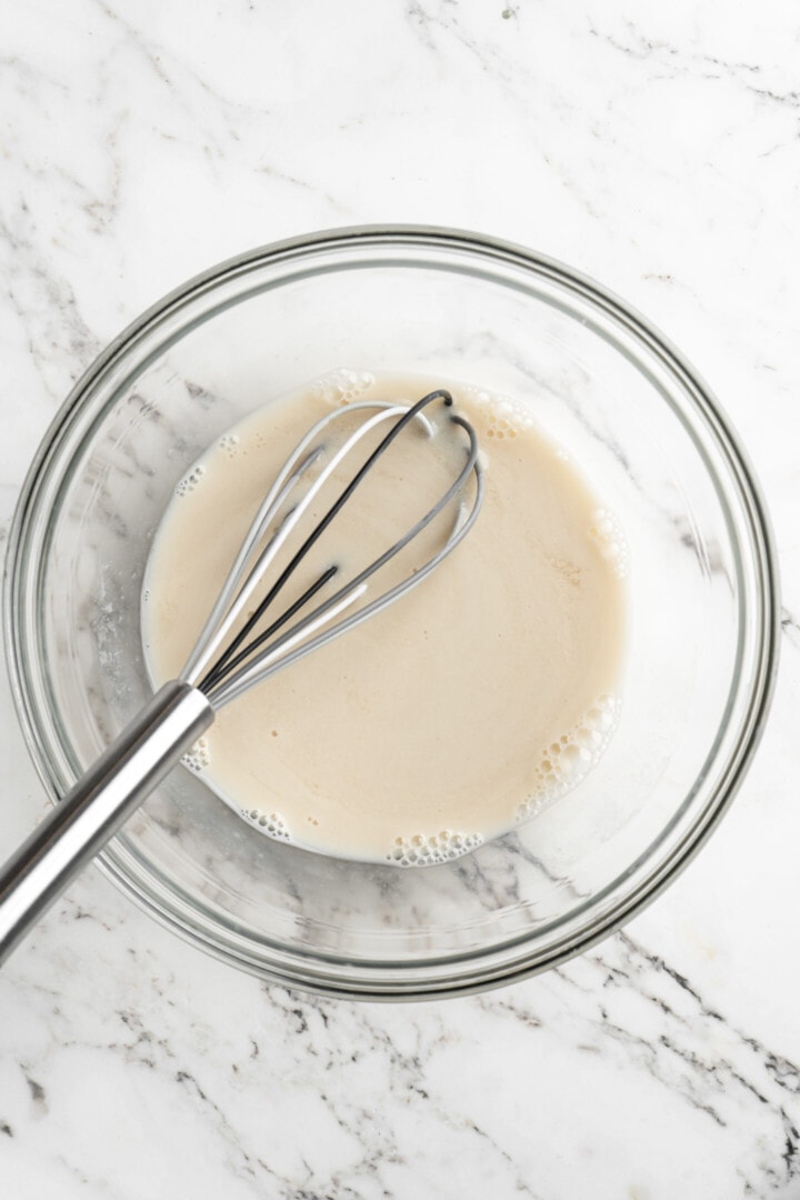 Overhead view of a mixing bowl with almond milk and a whisk.